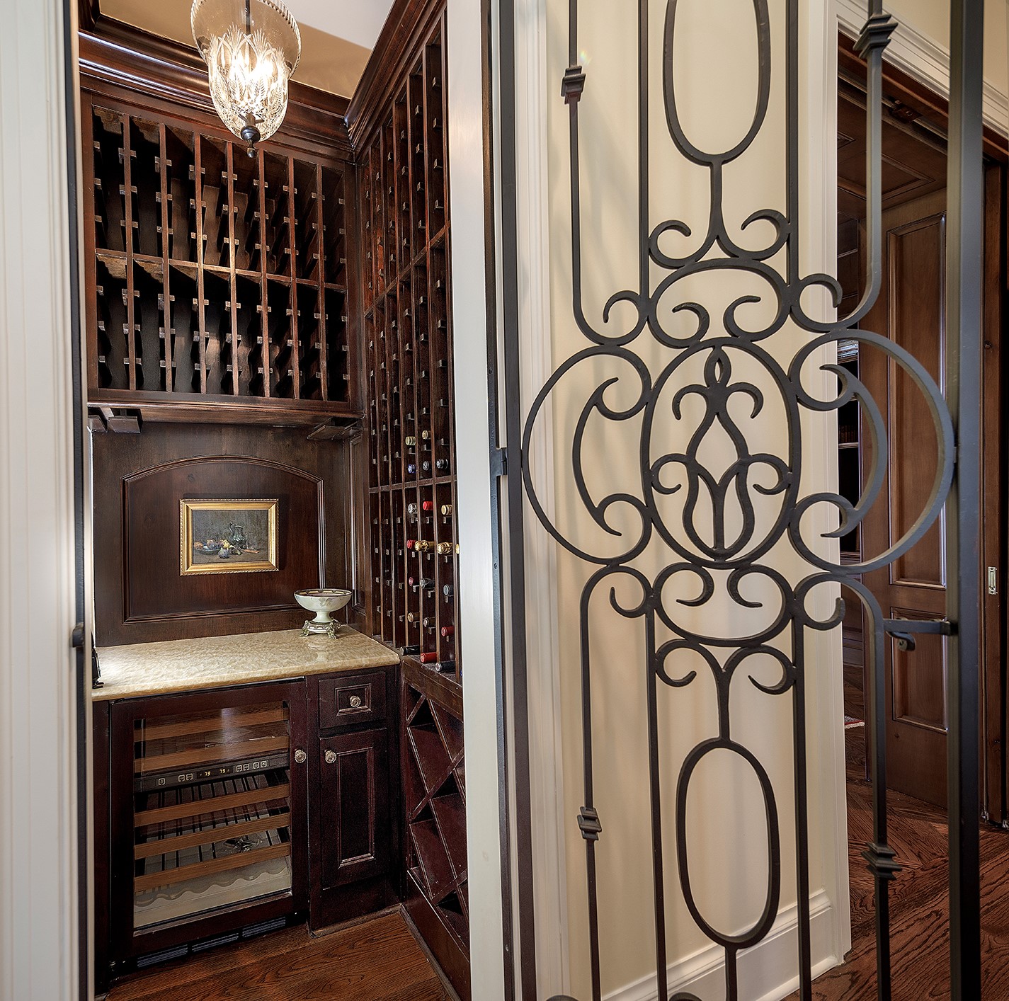 Wine room constructed from Smooth Alder, built-in SUB-ZERO wine refrigerator, Honey Onyx countertop, multiple racks, and custom wrought iron door. Waterford crystal pendant light. This room can be converted to an elevator.