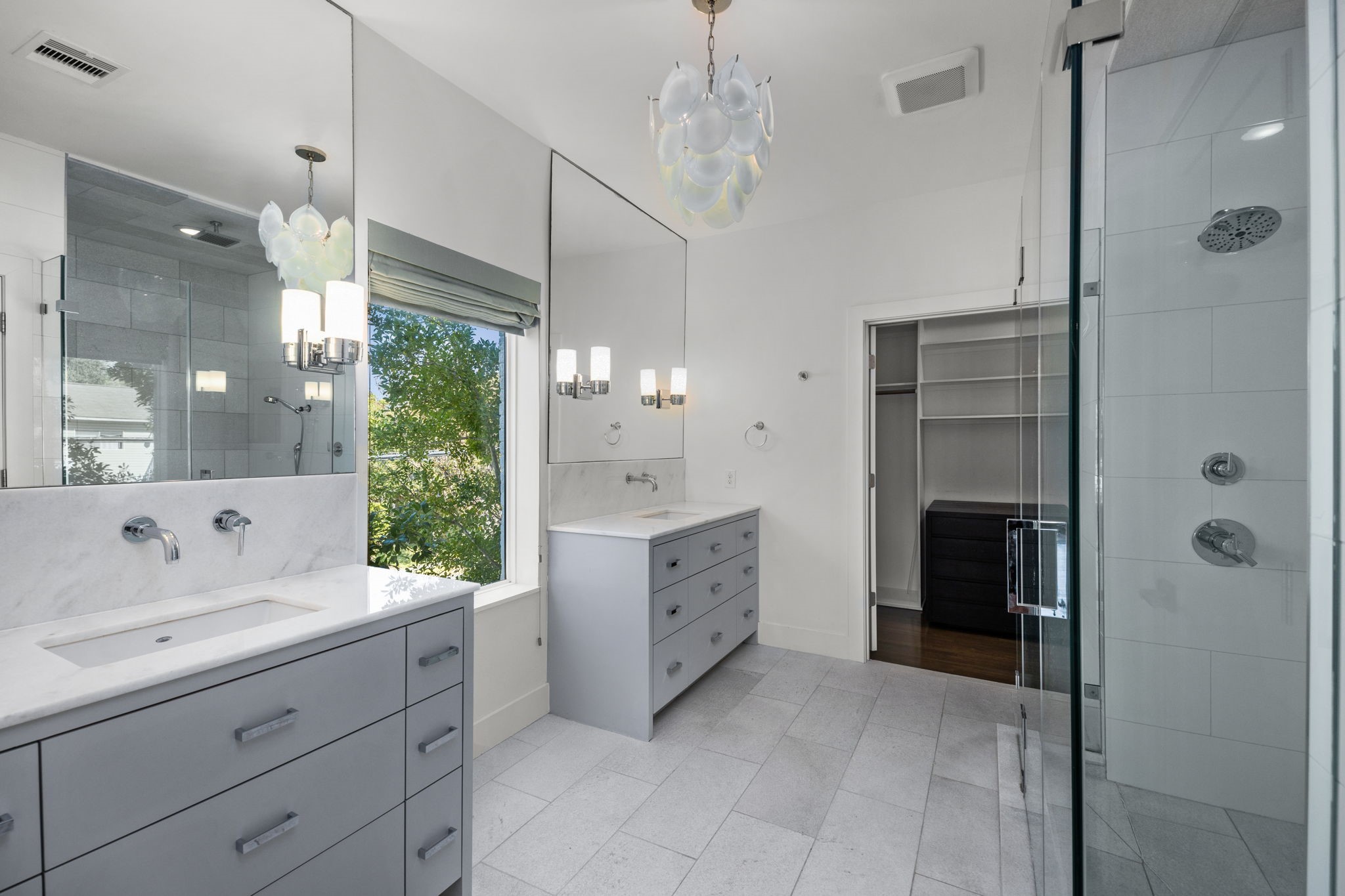 Exquisite primary bathroom features dual vanities, designer lighting, freestanding tub, and frameless glass shower.