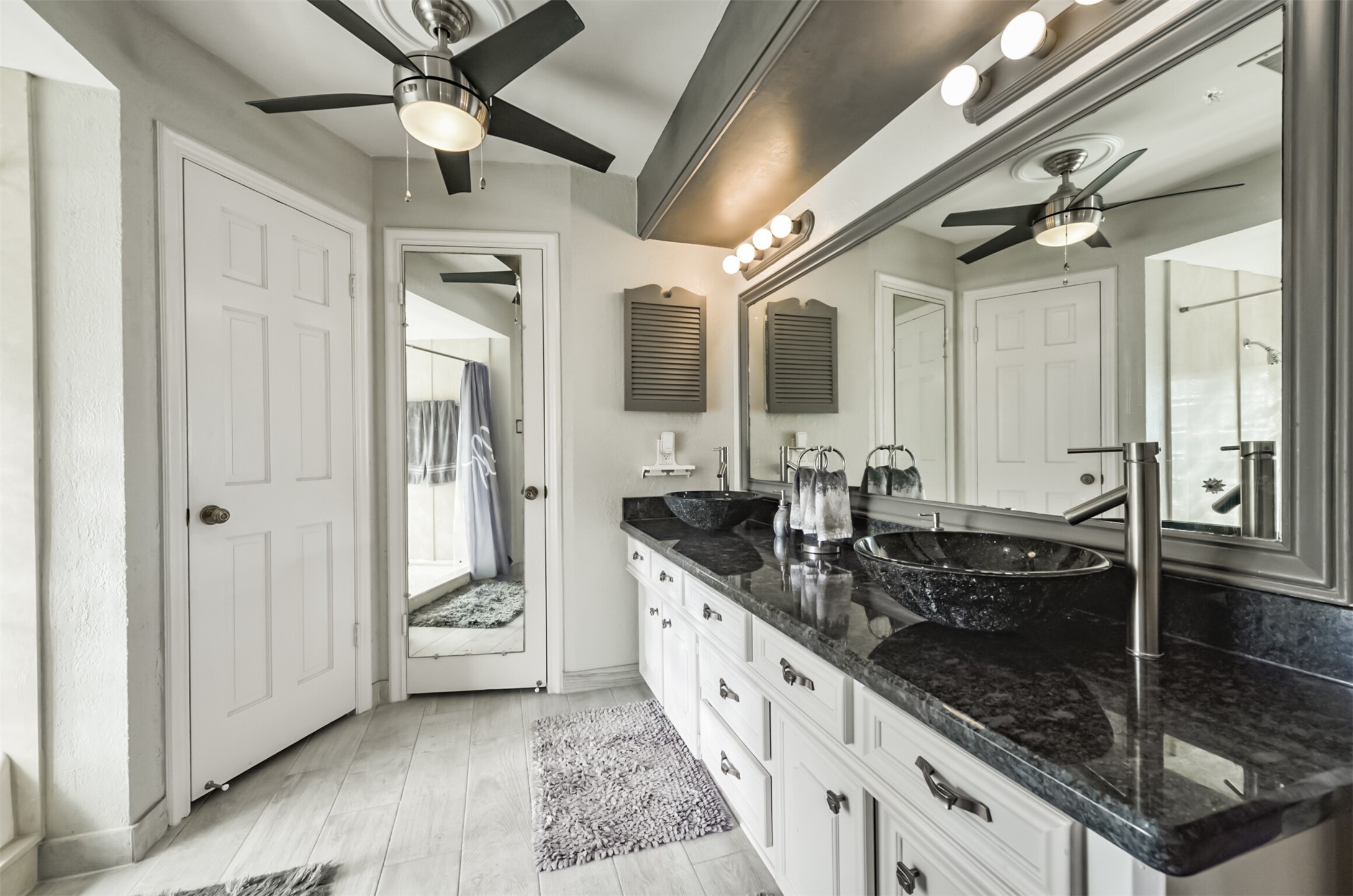 Double sinks, granite counter tops, a custom mirror and a ceiling fan in this elegant primary bathroom. The door with the mirror is the toilet.