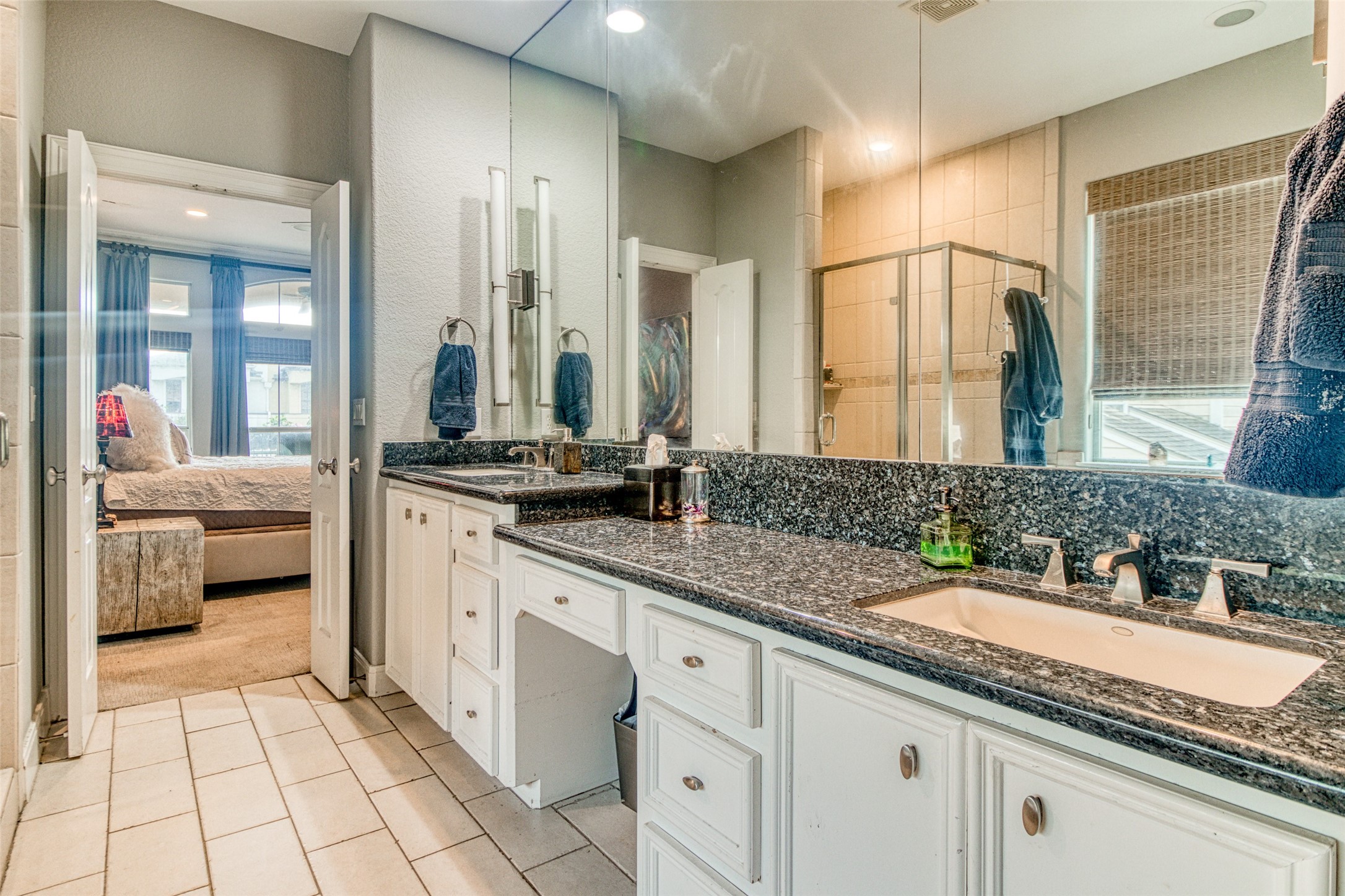This alternate view of the primary bathroom provides a glance at the separate glass-encased walk-in shower with floor-to-ceiling porcelain tile surround and built-in bench.  Note the dual-height vanities and the seating area for make-up in between.  Truly a homeowner's retreat!