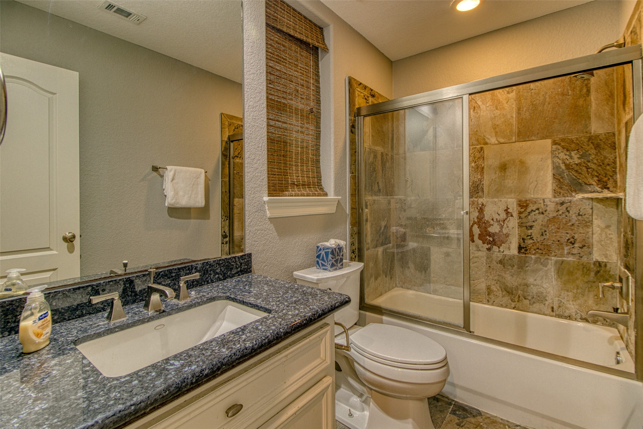The first-floor guest bathroom features slate floors and shower surround and shimmering granite countertop with undermount sink - an inviting and luxurious space for any guest.