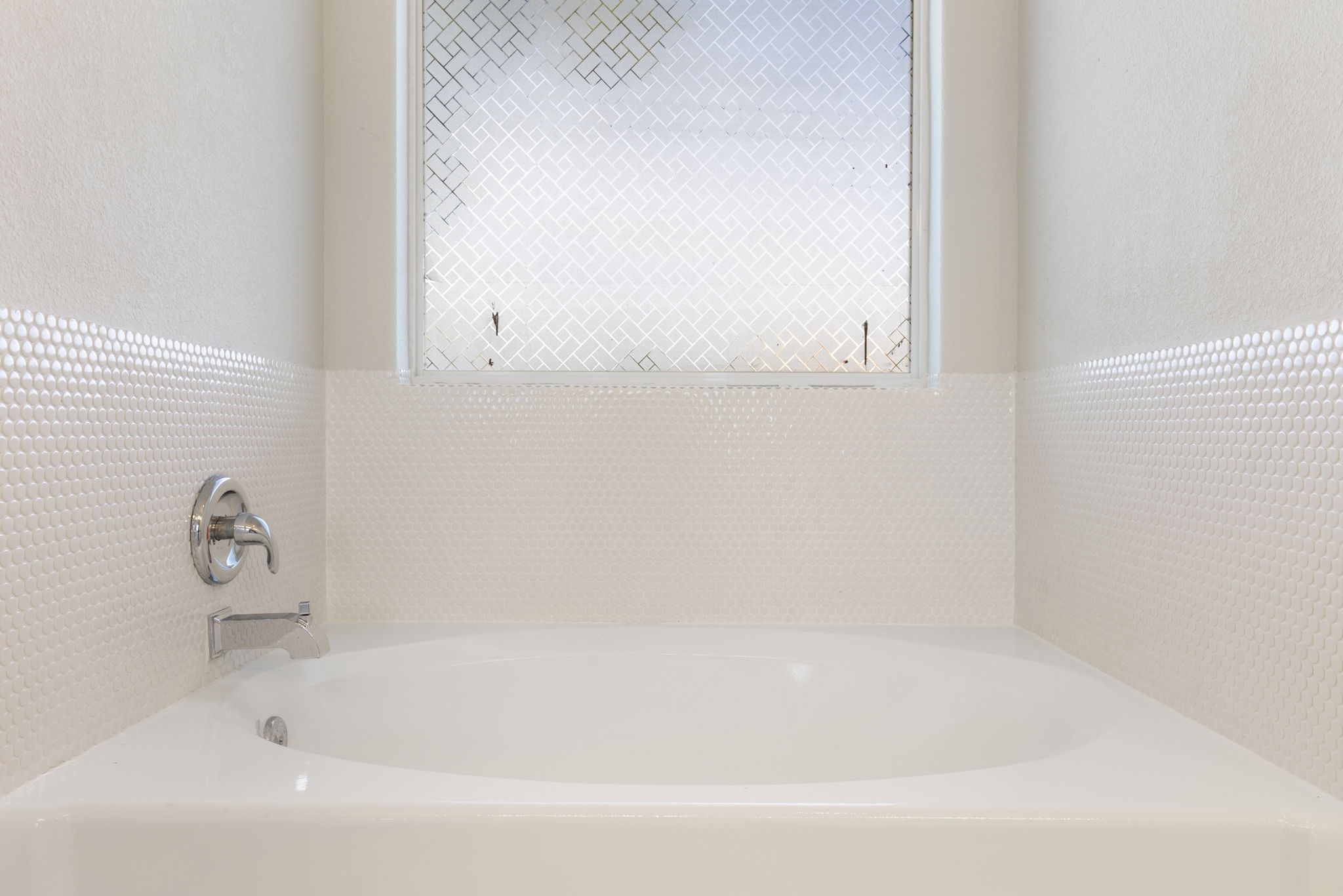 Relax in the soaking tub with decorative tile surround and patterned window for privacy.