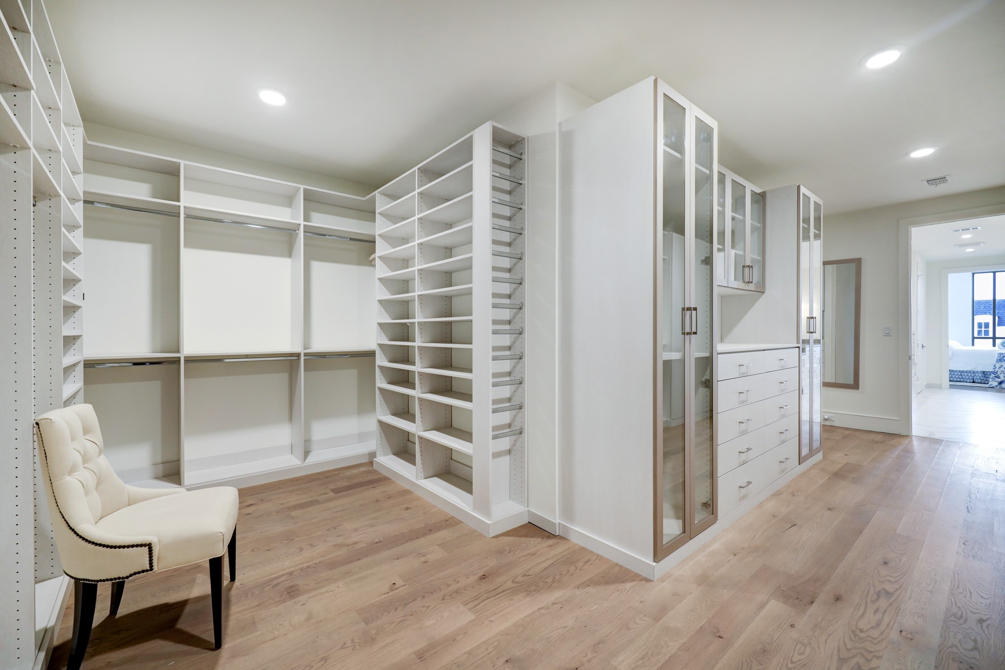 Another view of the PRIMARY CLOSET, this one showing the various sizes of the shelving provided, a packing station with drawers underneath and impressive glass front hanging closets.