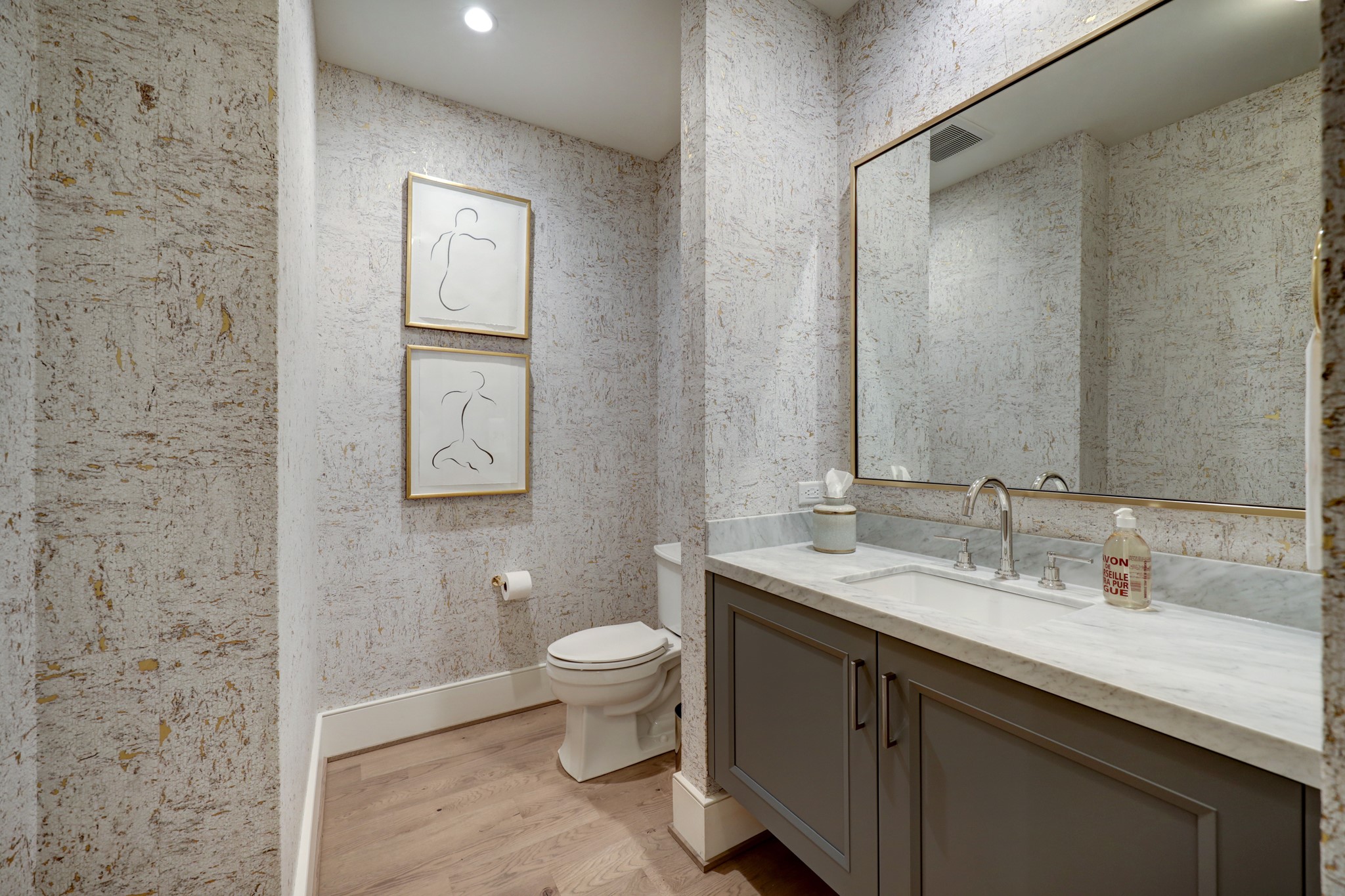 The over-sized formal POWDER ROOM features stone counter/backsplash with Kohler sink/cabinets below, elegant papered walls, hardwood flooring, base molding, decorative framed mirror/ Rohl fixtures and recessed lighting.