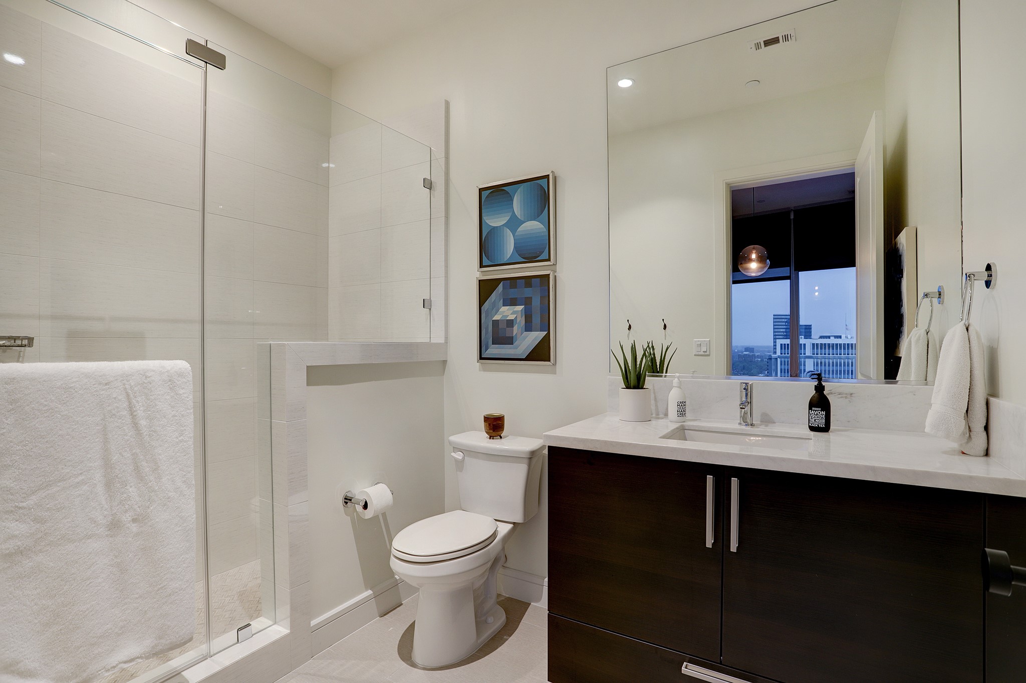 The EN SUITE BATH for the Guest Suite has a sizable walk-in shower clad in tile and a vanity with a quartz countertop.