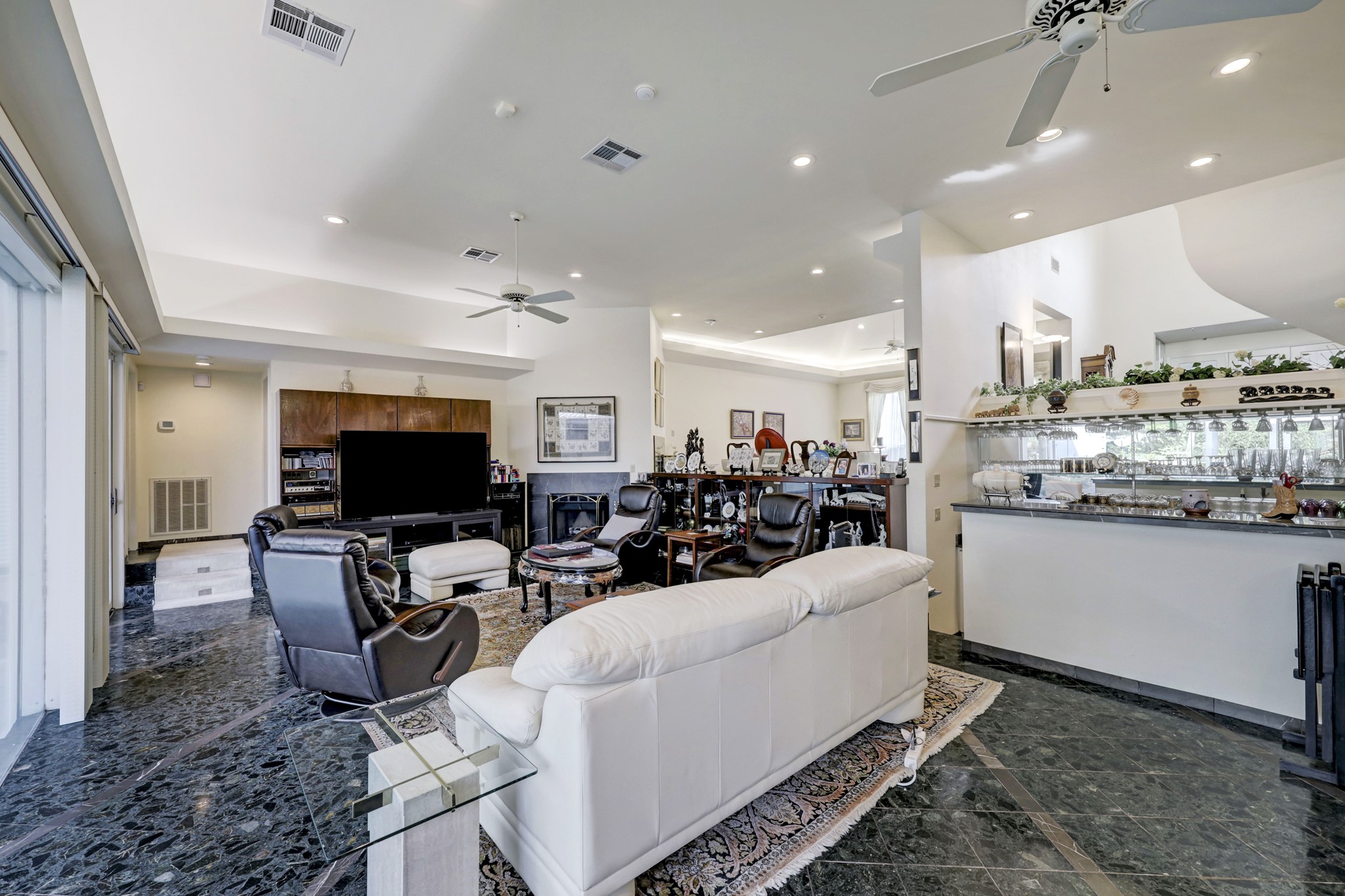 A wetbar with beverage fridge, built-in media cabinets, corner fireplace and views to the living room, kitchen and foyer are features of the massive family room that opens to the pool area. At the far end, steps lead to the primary suite and an ensuite bedroom.