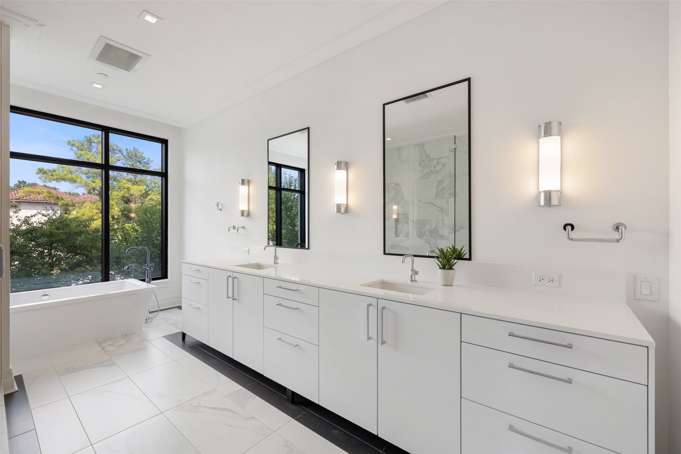 The Primary Bathroom with tree top views with a generous dual vanity, custom lighting and freestanding soaking tub.