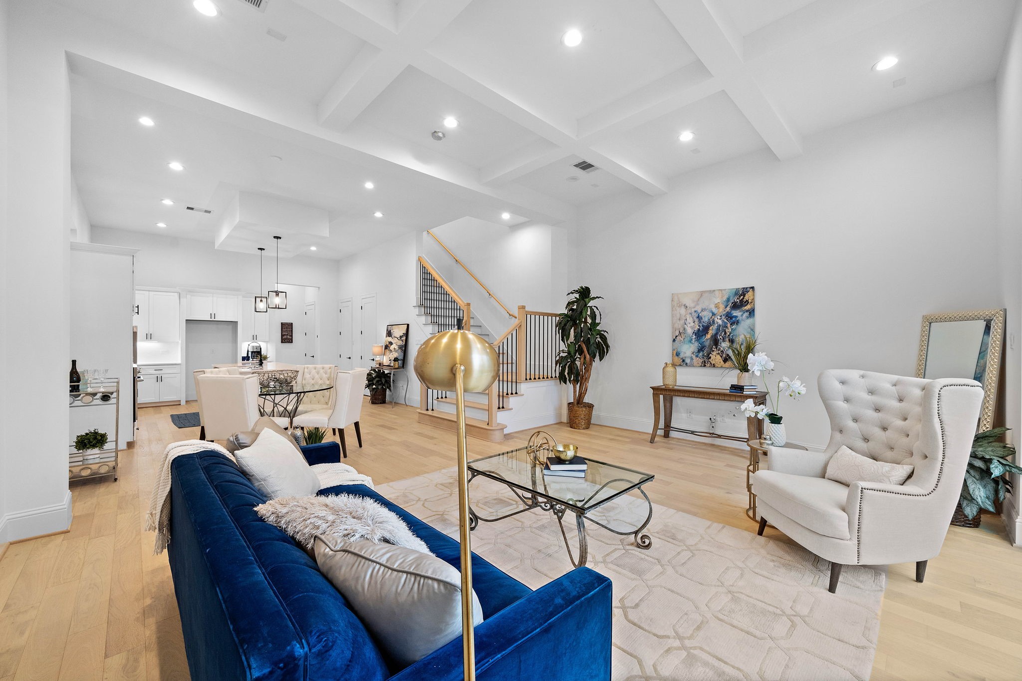 Spacious light and bright living with beamed ceiling, wide plank wood flooring, and wood stairway with wrought iron railing. (Photo is of a completed home, finishes are subject to change.)