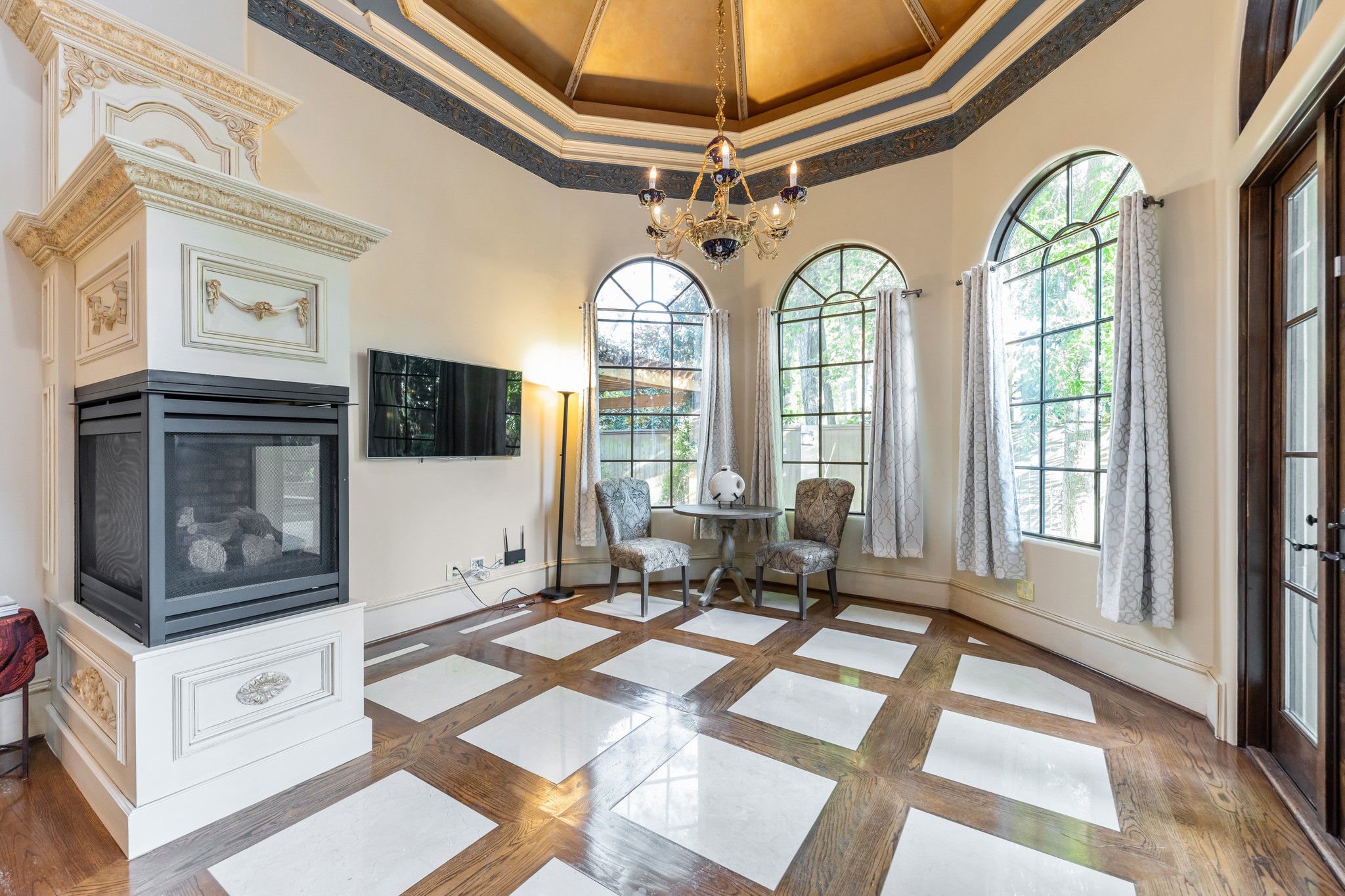 A luxurious sitting area with a custom designed domed ceiling, bay of large picture windows with picturesque views, 3-sided gas log fireplace, double doors lead to a relaxing primary private porch.