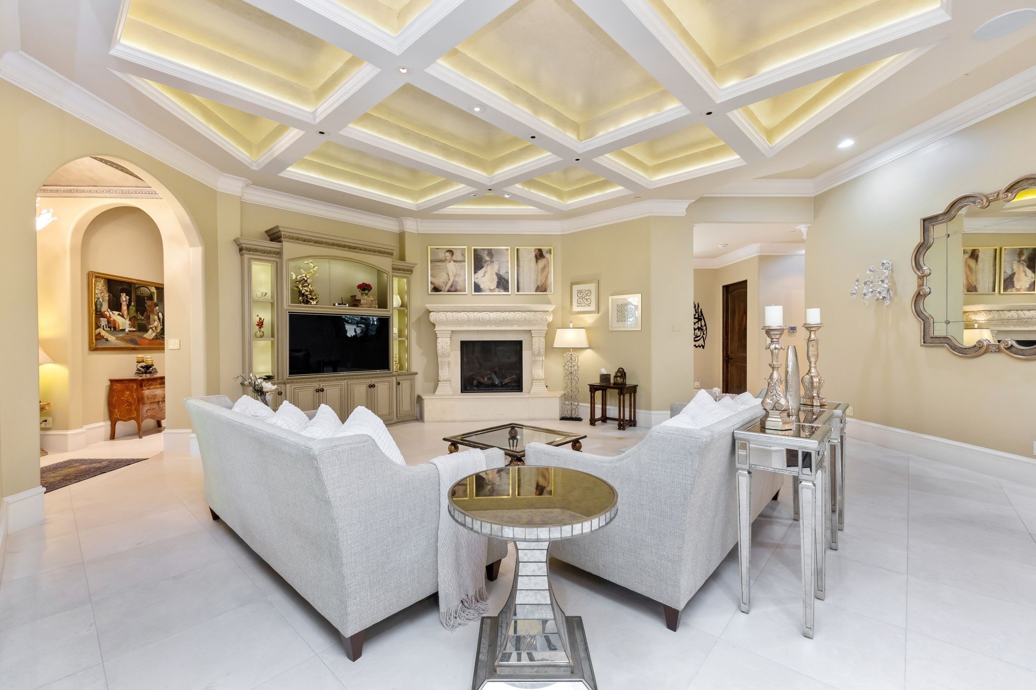 This lavish open concept family room features an impressive coffered ceiling, gas log fireplace with windows looking onto the warm and inviting covered veranda, which leads into the grand billiard room.