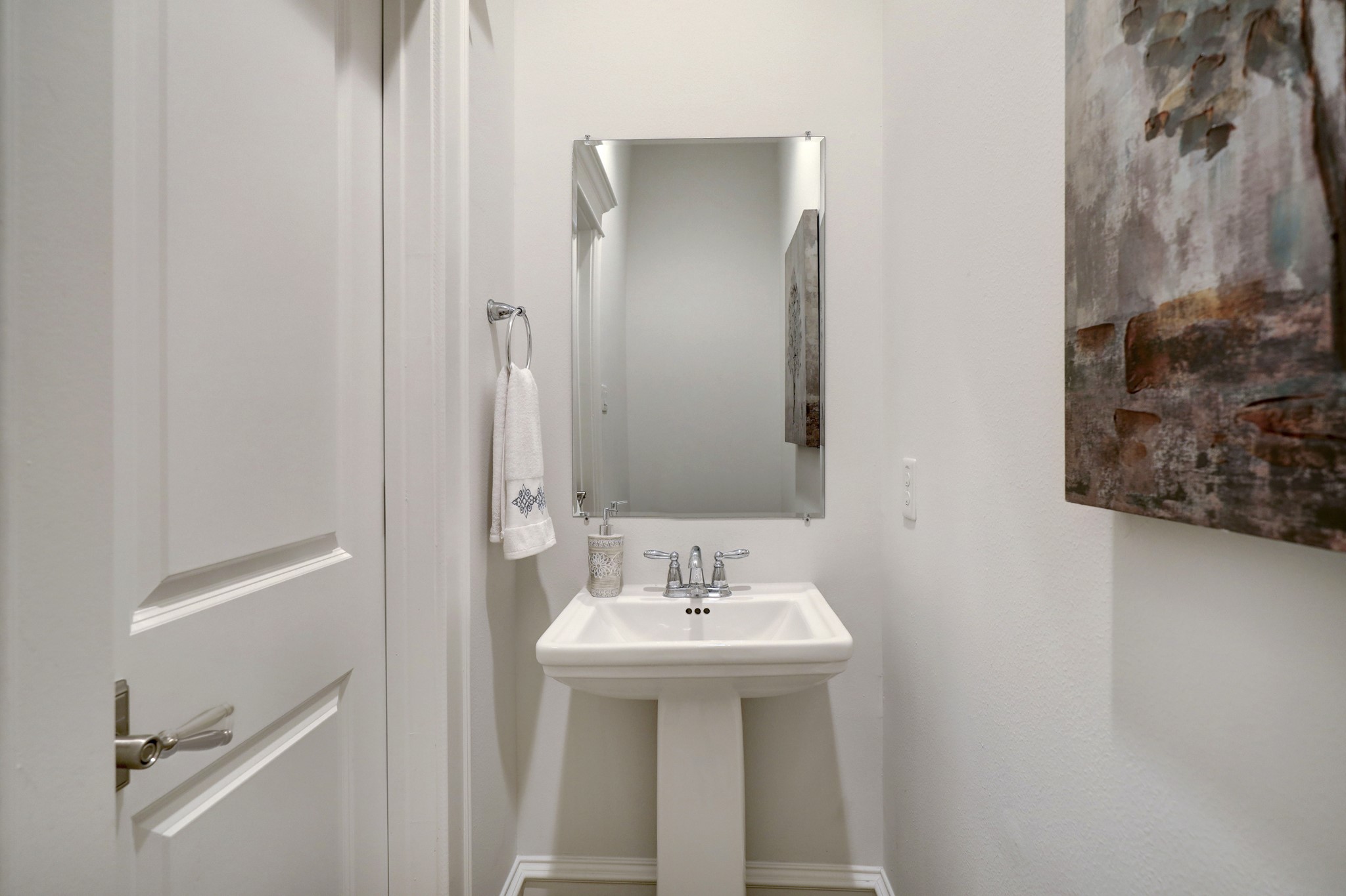 The powder room features an elegant pedestal sink. It's just beyond the kitchen, perfect for friends and guests.