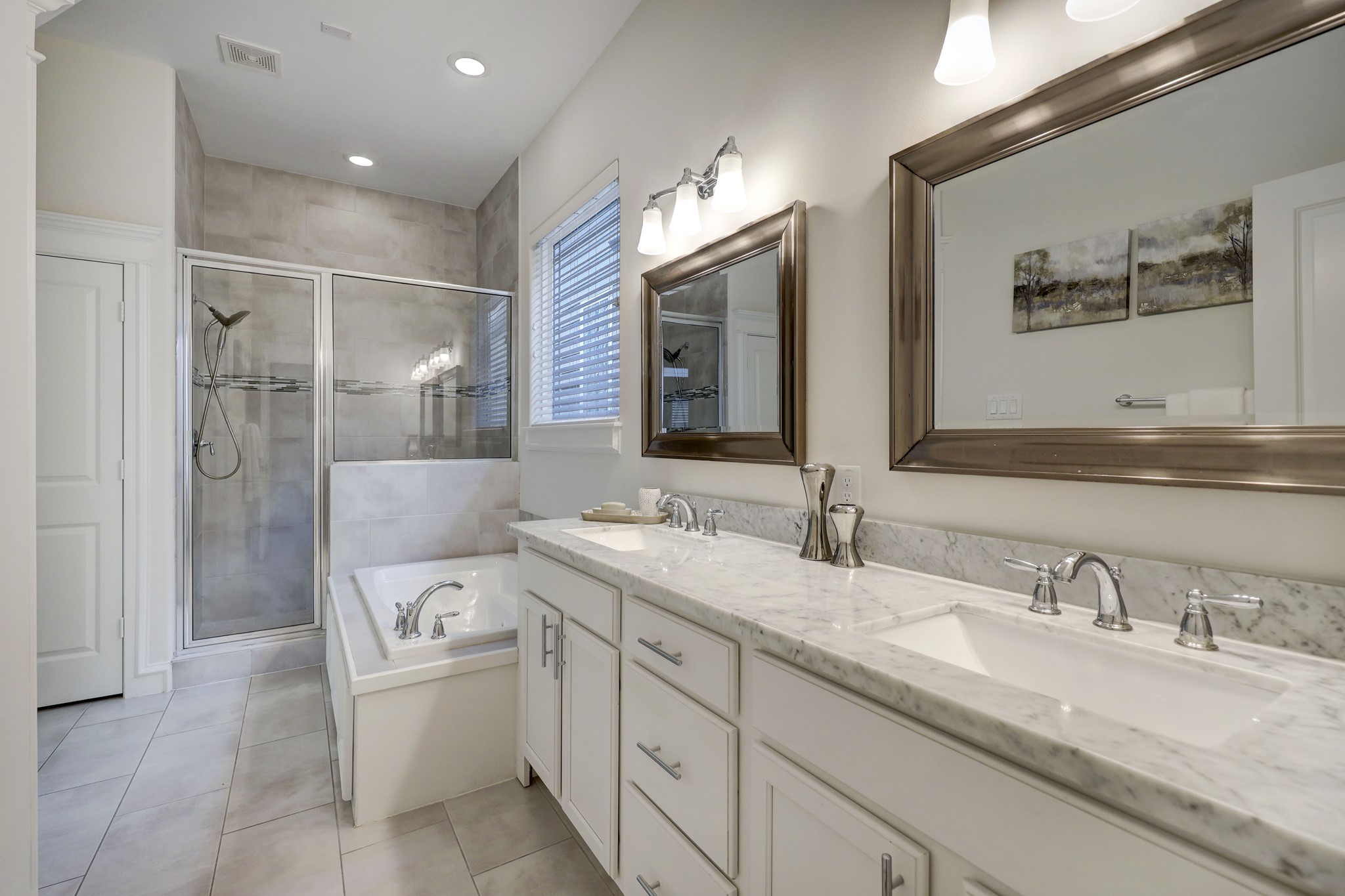 Framed mirrors, elegant lighting, and chrome hardware lend a luxurious feel to the glass-enclosed shower.
