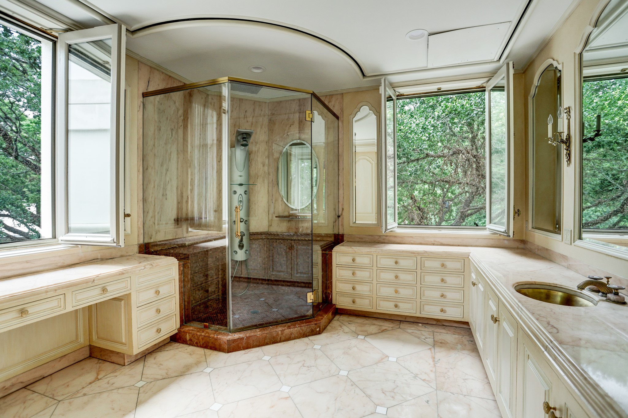 A second primary bath boasts an immense Kohler deep whirlpool soaking tub with padded headrests and hand-shower attachment for ultimate rest and relaxation. Behind the soaking tub is another expansive walk-in shower with marble tiled accents and glass enclosure with frameless glass door. Notice the under-mounted gilded basin situated on the gorgeous slab marble counter and the marble tile floor with contrasting inlaid marble accent panels and borders.