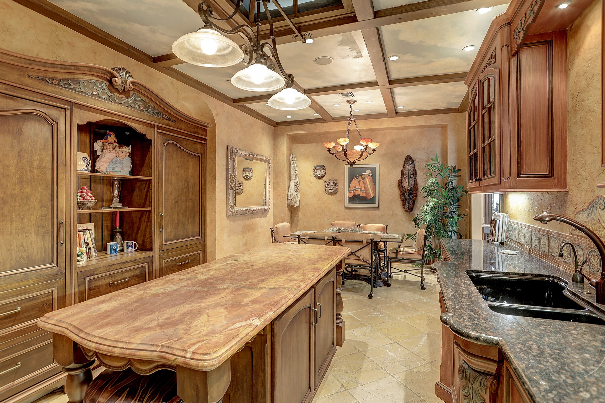 There is a refectory table-style island with marble deck, seating and storage.  The bull nose granite countertops have mosaic travertine tile backsplash with antique Italian mythological tile inserts.