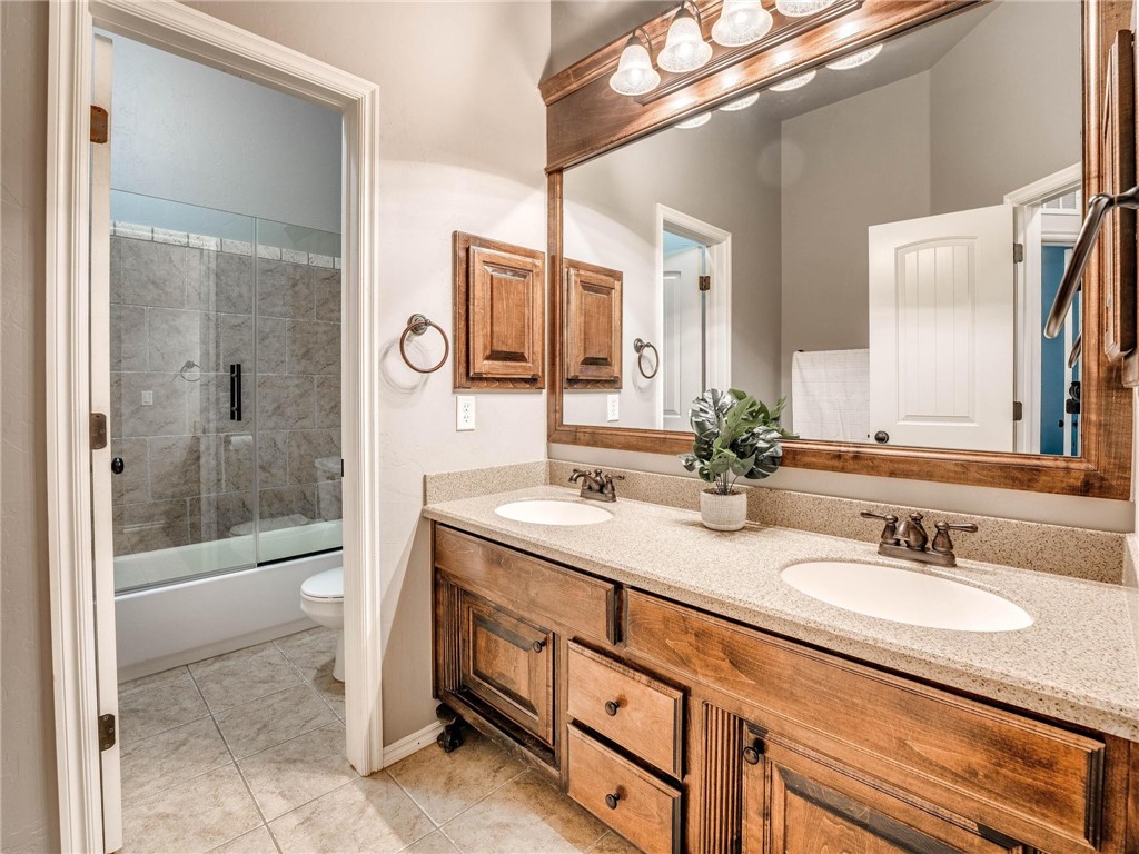 4311 Kensal Rise Place, Norman, OK 73072 full bathroom with tile floors, dual mirrors, his and her basins, his and hers large vanities, enclosed tub / shower combo, and toilet