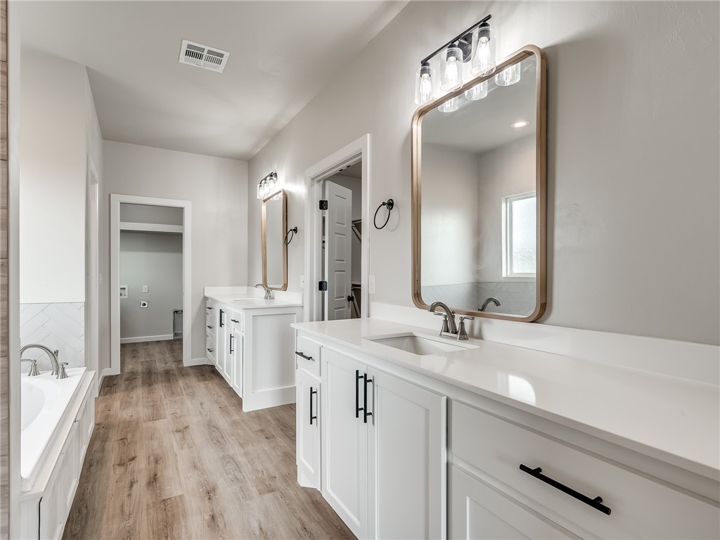1005 Heritage Hills Drive, Tuttle, OK 73089 bathroom with hardwood flooring, double vanity, dual mirrors, and a bathtub