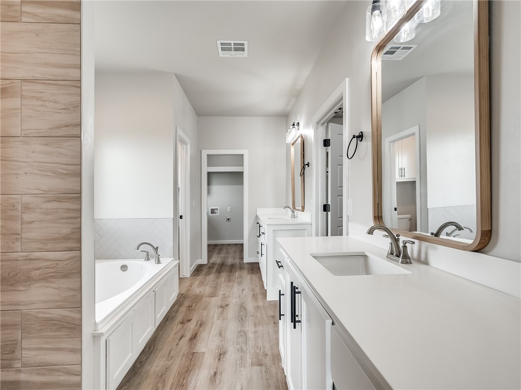 1005 Heritage Hills Drive, Tuttle, OK 73089 bathroom featuring hardwood floors, dual vanity, dual mirrors, and a bathtub