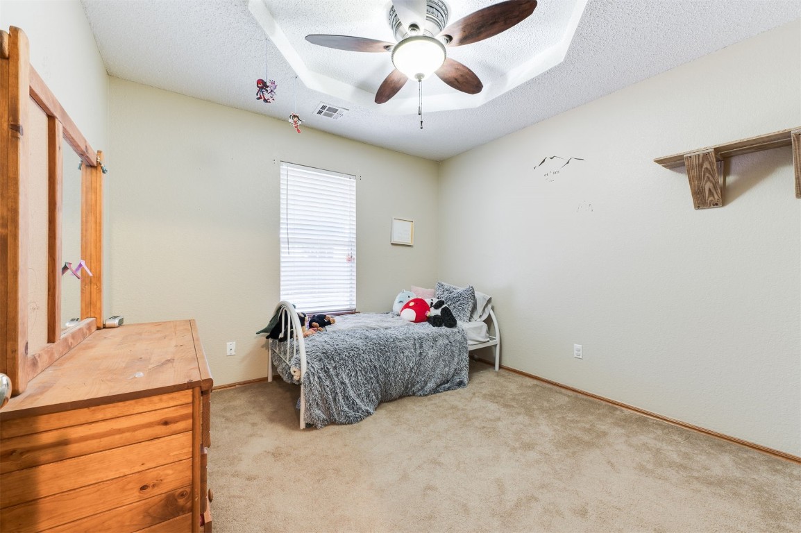 9306 Buttonfield Avenue, Moore, OK 73160 carpeted bedroom with ceiling fan, a tray ceiling, and a textured ceiling