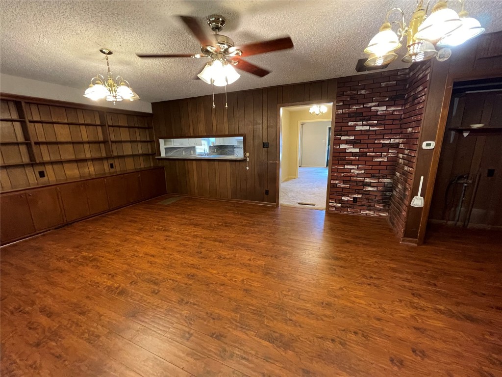 1815 Park Avenue, Chickasha, OK 73067-4505 hardwood floored empty room featuring a textured ceiling, wooden walls, brick wall, and ceiling fan