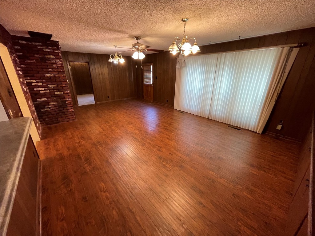 1815 Park Avenue, Chickasha, OK 73067-4505 living room with brick wall, a textured ceiling, dark hardwood floors, wood walls, and ceiling fan