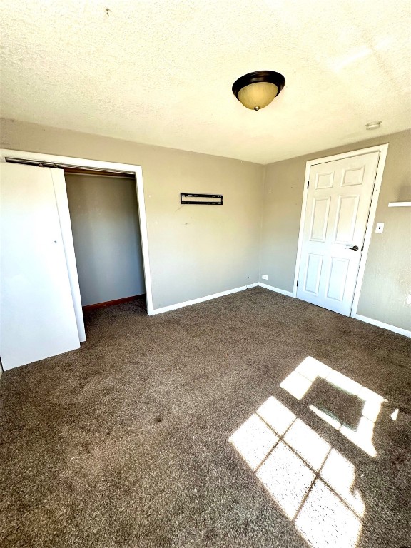 1208 S Grand, Ninnekah, OK 73067 unfurnished bedroom with dark colored carpet, a textured ceiling, and a closet
