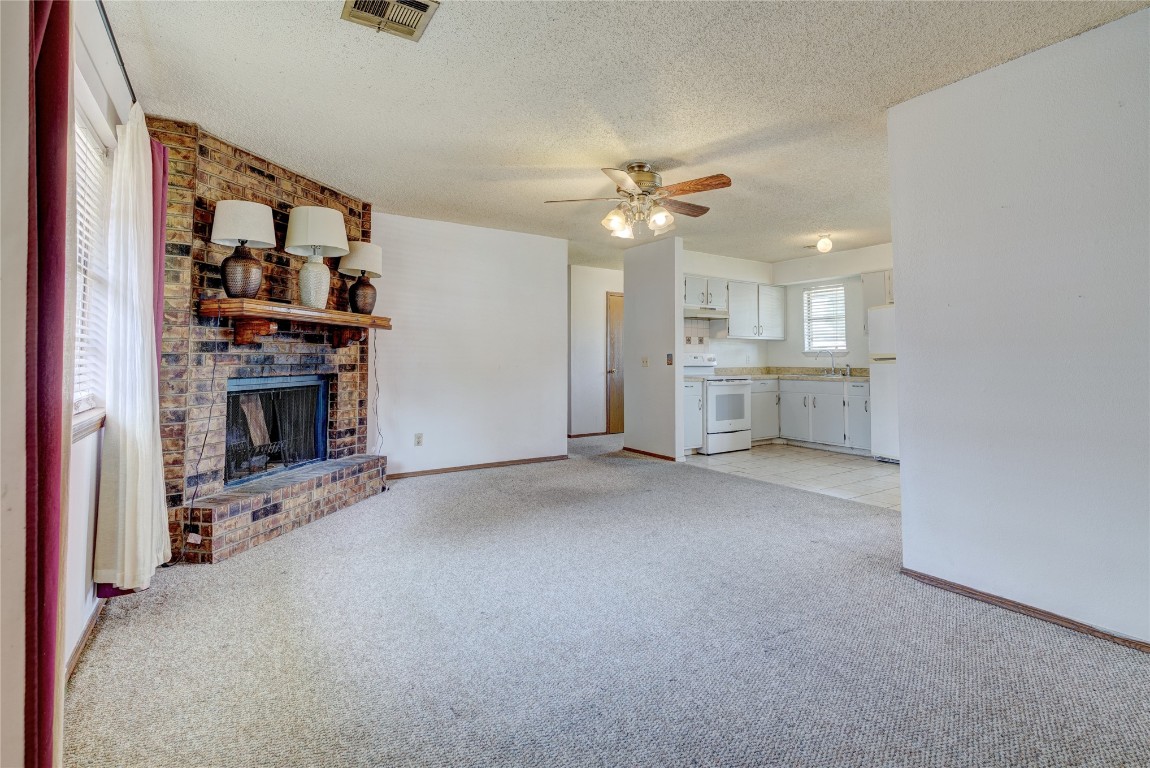 1142 W Gladys Way, Mustang, OK 73064 living room with a textured ceiling, brick wall, light carpet, ceiling fan, and a fireplace