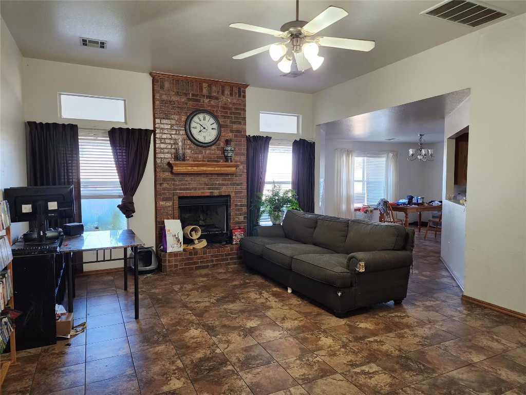 723 E Forest Court Lane, Mustang, OK 73064 living room with ceiling fan with notable chandelier, dark tile flooring, a brick fireplace, and brick wall