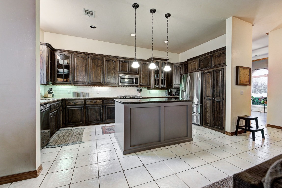 1304 Polly Way, Mustang, OK 73064 kitchen featuring appliances with stainless steel finishes, pendant lighting, dark brown cabinetry, tasteful backsplash, and a kitchen island