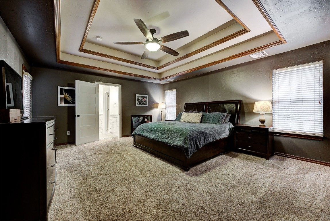 1304 Polly Way, Mustang, OK 73064 bedroom with light carpet, a tray ceiling, ceiling fan, and crown molding