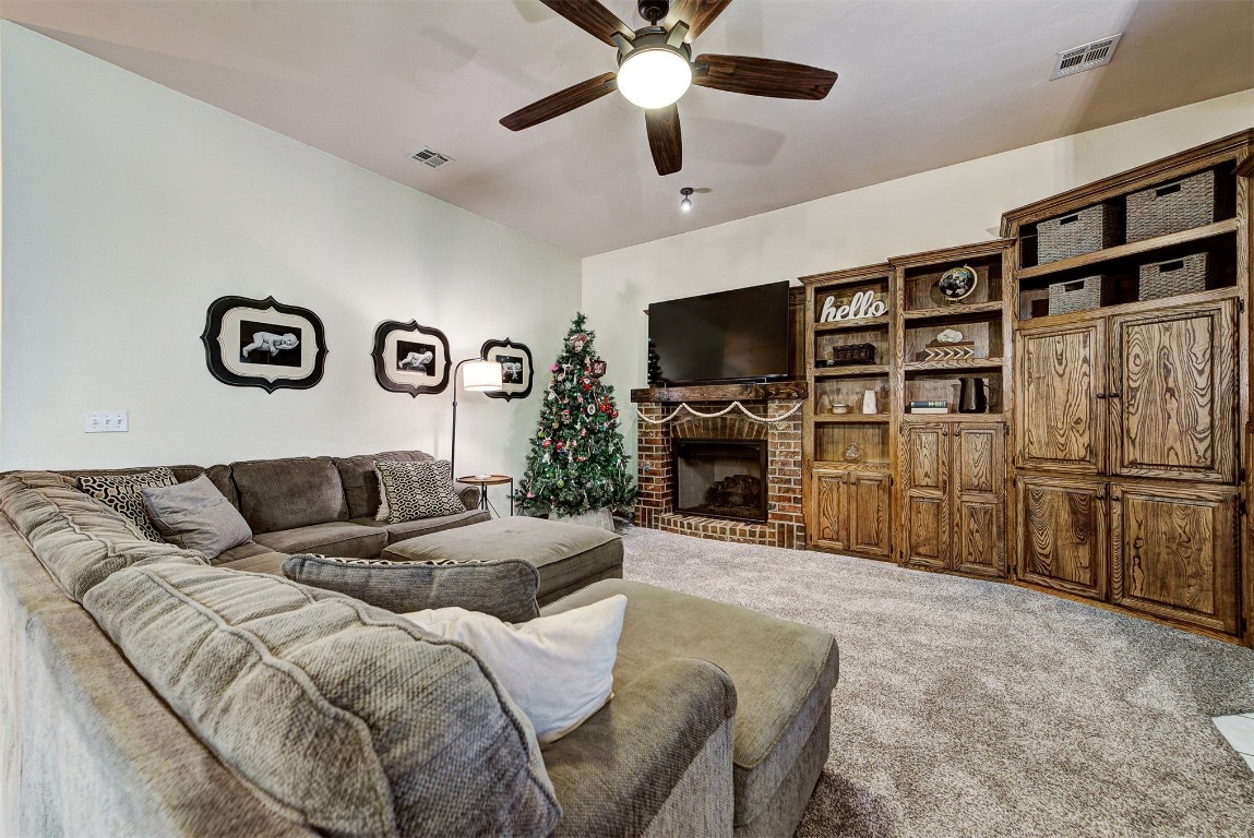 1304 Polly Way, Mustang, OK 73064 living room featuring a brick fireplace, ceiling fan, and carpet flooring