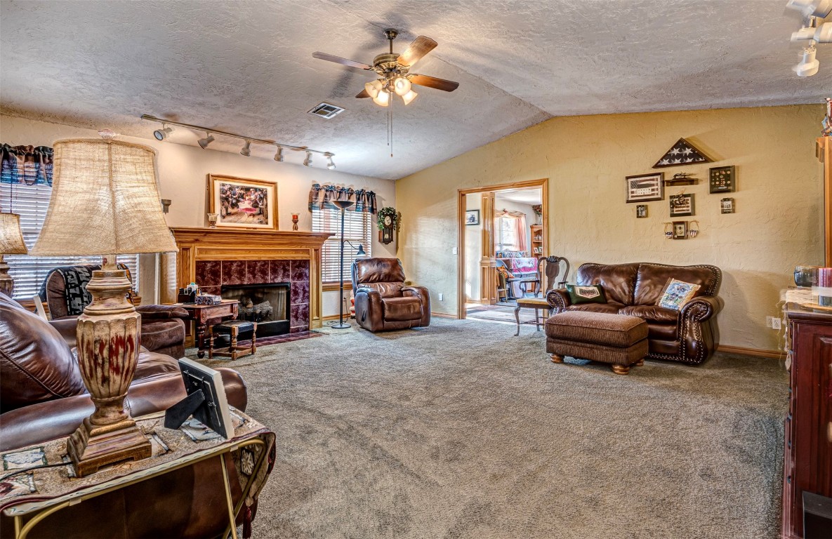 3735 Janet Circle, Mustang, OK 73064 living room with track lighting, carpet, ceiling fan, a tile fireplace, and a textured ceiling