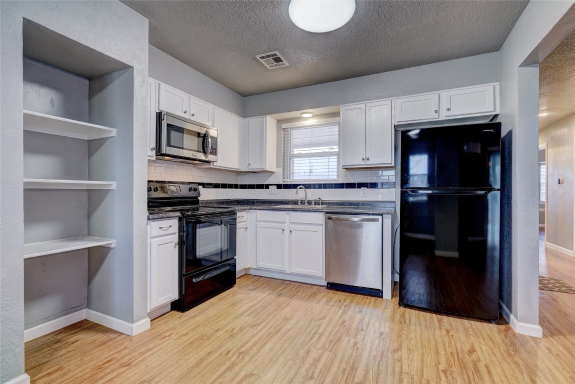 44 SE 57th Street, Oklahoma City, OK 73129 kitchen with light wood-type flooring, black appliances, backsplash, and white cabinets