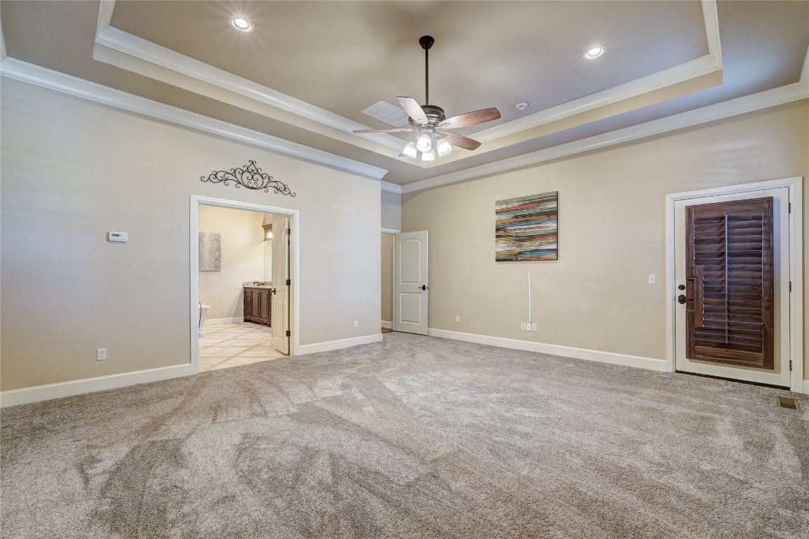 2355 La Belle Rue, Edmond, OK 73034 unfurnished bedroom with a raised ceiling, connected bathroom, crown molding, ceiling fan, and light colored carpet