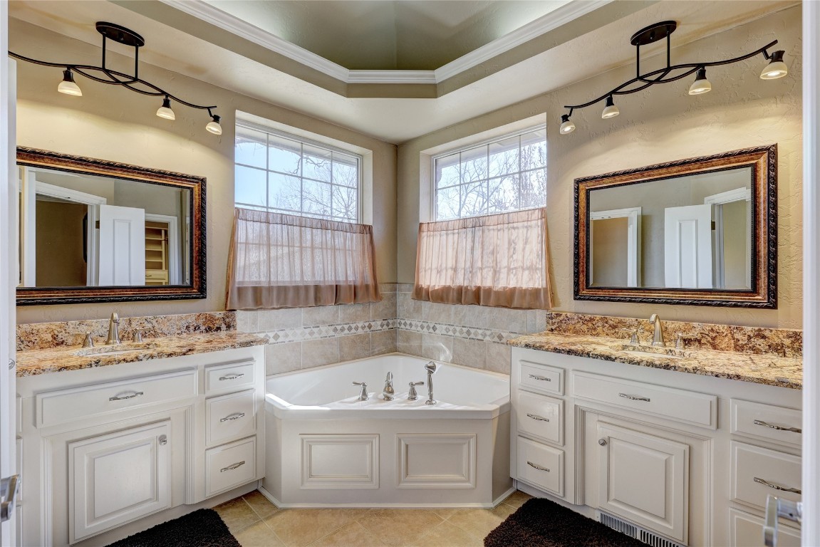 1941 Oak Creek Terrace, Edmond, OK 73034 bathroom featuring a tub, vanity, crown molding, tile floors, and a tray ceiling
