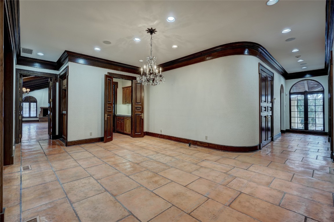 3900 S Bryant Avenue, Edmond, OK 73013 empty room with light tile flooring, crown molding, a notable chandelier, and french doors