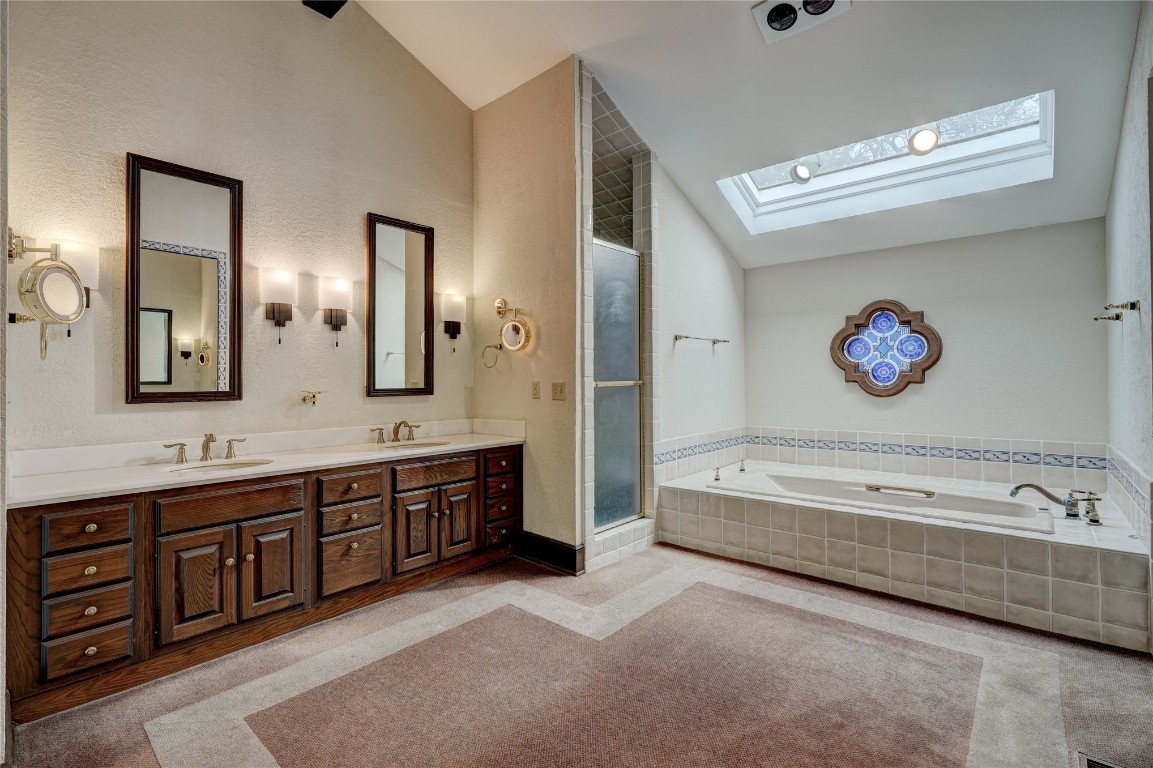 3900 S Bryant Avenue, Edmond, OK 73013 bathroom with dual vanity, vaulted ceiling with skylight, and independent shower and bath
