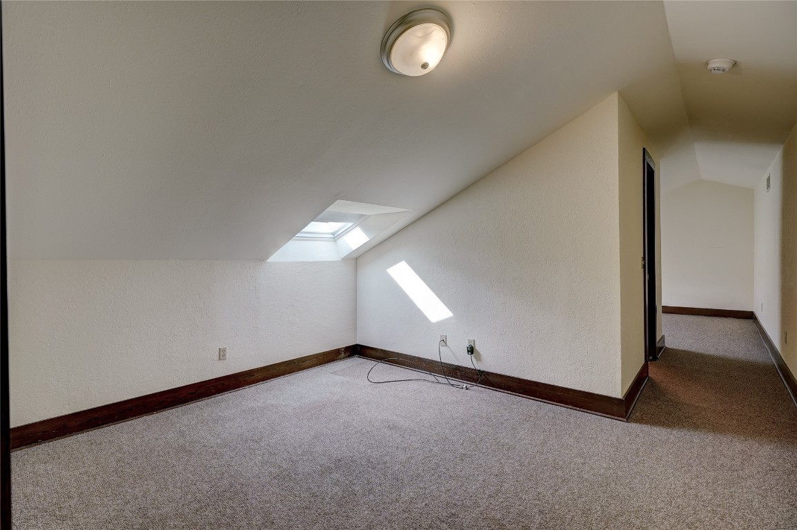 3900 S Bryant Avenue, Edmond, OK 73013 additional living space with dark carpet and vaulted ceiling with skylight