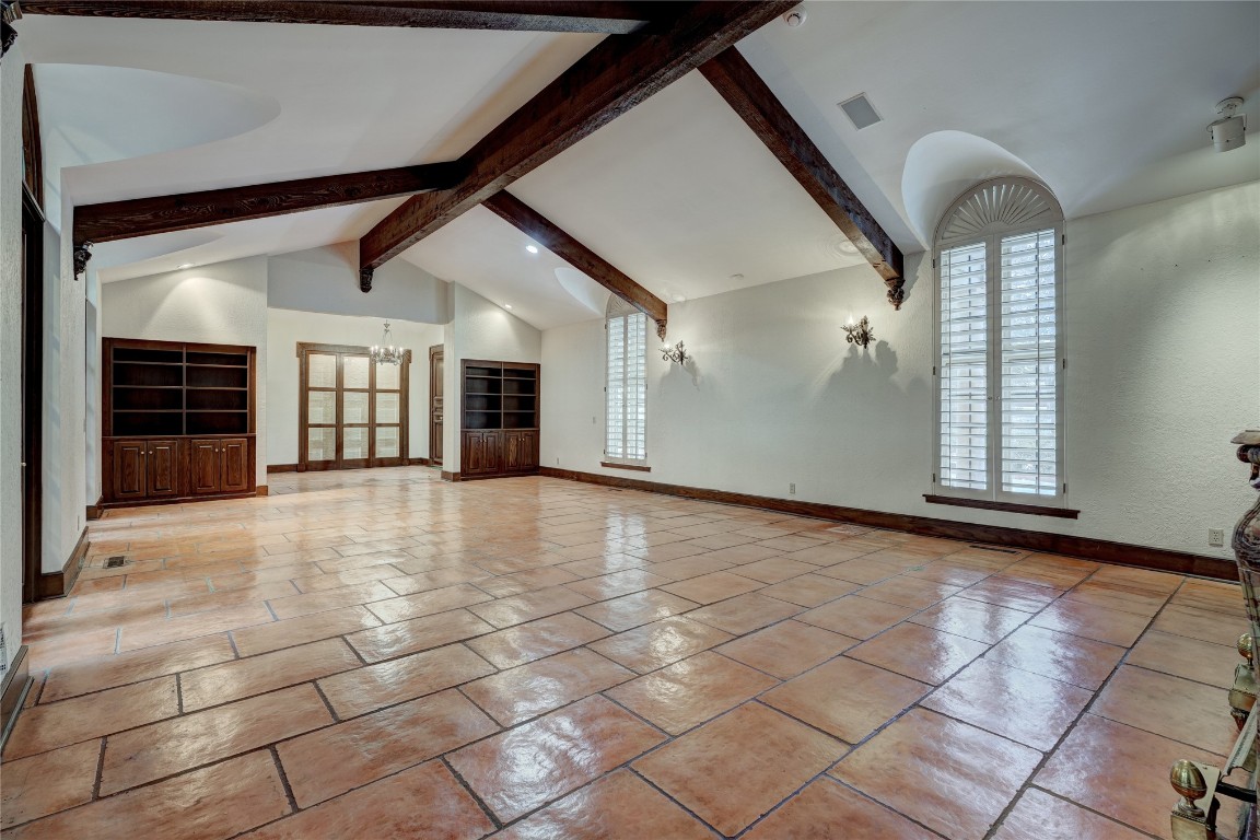 3900 S Bryant Avenue, Edmond, OK 73013 unfurnished living room featuring a chandelier, high vaulted ceiling, light tile floors, and beam ceiling