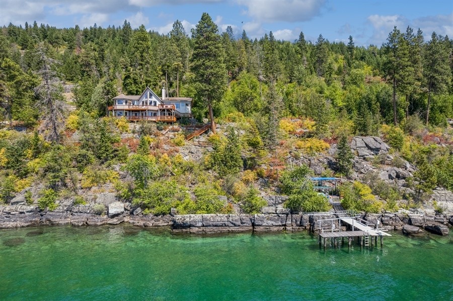 Stunning East Shore Property on Flathead Lake - 429 feet of shoreline, beach, and rock outcroppings.  This waterfront property is on 2.86 acres with a stylish 4 bedroom, 3 bath home with thoughtful design details such as lots of natural light, incredible views from every room, as well as the rock you see in the interior of the home being handpicked from the property.  The lower level hosts an apartment with its own entrance.  The dock provides easy access to the lake, making activities such as boating, fishing and swimming relaxing and enjoyable.  Above the dock is a covered grilling, outdoor kitchen/dining area providing a fantastic and pleasant space.  The decks off the living rooms of the home are also set up for grilling and entertaining.  Minutes away from the town of Bigfork, a lovely, year-round resort village that is brimming with art galleries, fine restaurants, Eagle Bend Golf Course, and live theatre. This property has been a successful VRBO for the last two years.  Recent updates include new paint, flooring, and additional decking.  A fun fact is that on some maps this property is home to the ‘Fishing Rock’ for which the road is named.  This property is also an easy drive to Glacier Park, Blacktail Ski Resort, Big Mountain Ski Resort, Glacier International Airport, and many more of Flathead Valley’s amenities. Call Deb Johnson at (406) 471-4614 or your real estate professional.