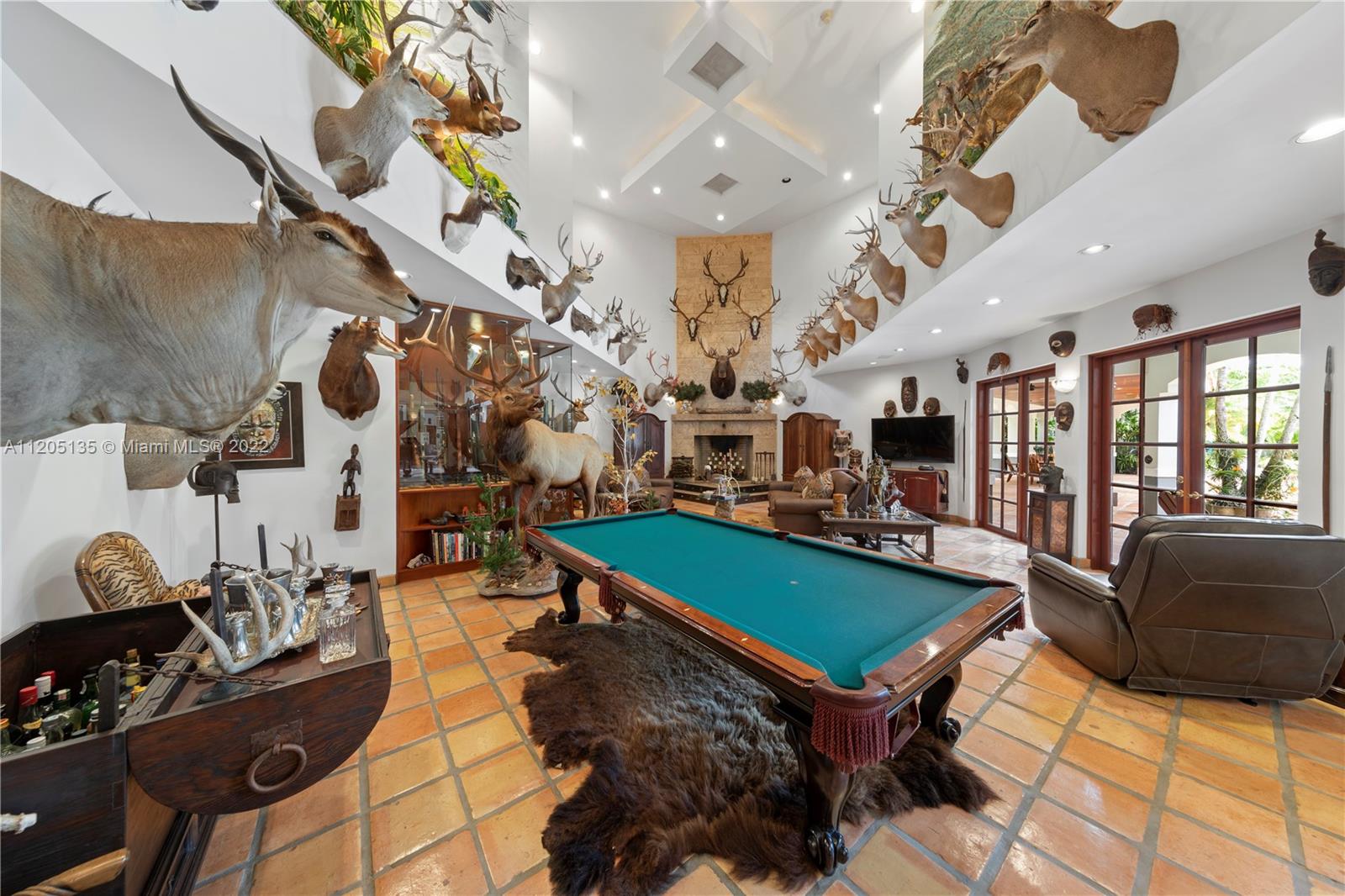 The game room~ There are so many options for this space with its 24' ceiling height, custom display units, lighting from all angles. The stately wood burning fireplace centers this room and like the rest of this villa, there's a warmth to the space..