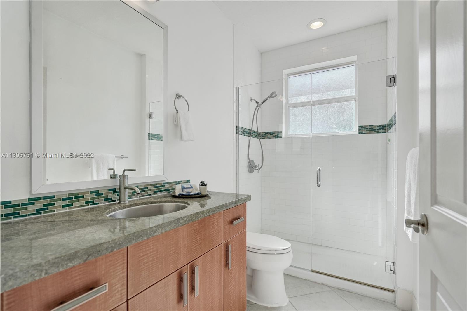 Bathroom #2 with modern wood vanities, marble counters, mosaic backsplash, silver mirror, seamless glass shower.