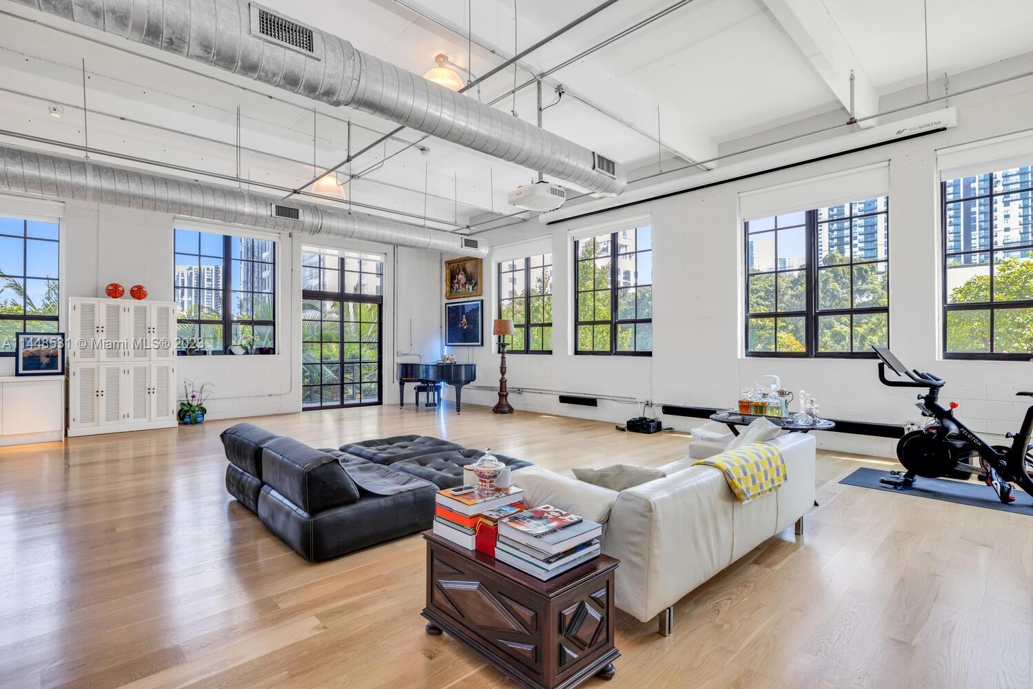Discover the epitome of urban living in this exceptional New York-style loft condo, a rarity in Miami's Arts & Entertainment district - minutes away from Wynwood, Downtown, Edgewater and the Design District. With its unique combination of industrial charm and contemporary elegance, this corner unit is a true gem that is perfect for entertaining. 
This home boasts soaring 15-foot ceilings, oversized windows with electric blinds allowing in an abundance of natural light, beautiful light oak hardwood floors, renovated bathrooms and kitchen, and an impressive movie projector screen measuring 13' x 18'. One parking space with EV charger is included with room to add a lift for a second vehicle.