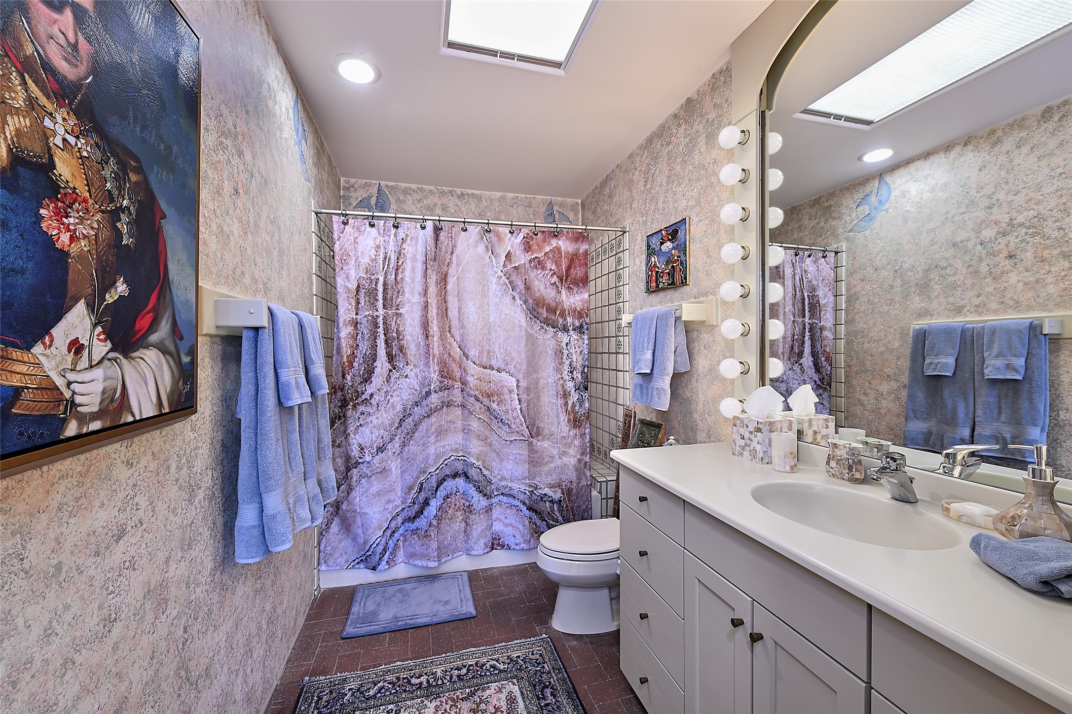 This spacious bath also offers a generous vanity with a large mirror and cosmetic lighting; faux-finished walls and the subdued ceramic tile of the tub shower create a unique, calming palette.