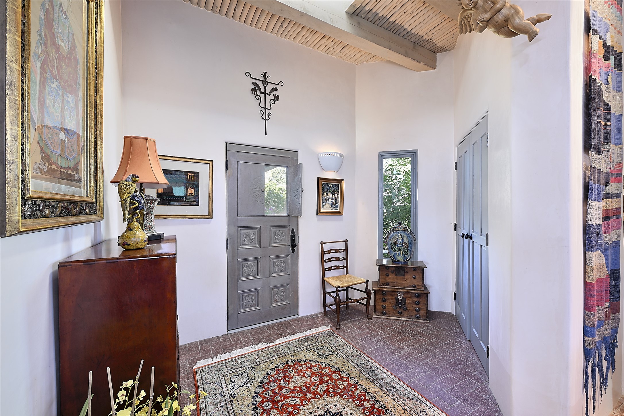 Beneath a tall skylit ceiling of latillas and beams, this small charming foyer includes a coat closet and serves as an auxiliary entrance to the home.