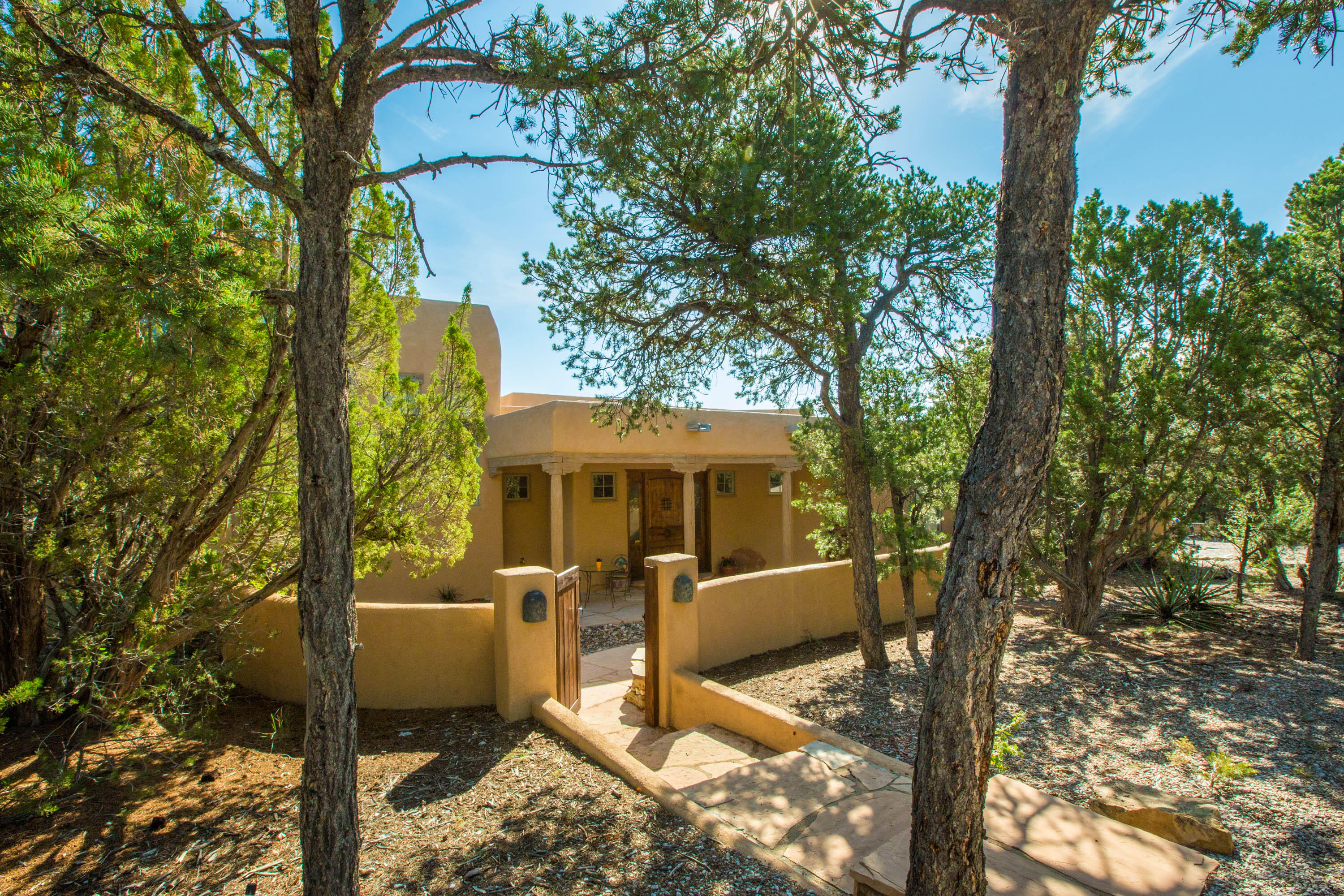 This beautiful custom home provides seclusion among the trees on a generous 3.08 acre lot. The fenced entry courtyard is the perfect entry into this open concept southwest style home. Solid wood Santa Fe doors, beamed ceilings and a kiva fireplace in the great room open to an immaculate kitchen perfect for entertaining. With an abundance of cabinetry, large pantry, granite counter tops, double oven with a warming drawer, gas cooktop and an additional prep sink, this kitchen checks all the boxes - not to mention the views to patio and backyard it provides. The formal dining area has its own built in buffet with extra storage and domed ceiling. The owner's suite boasts vigas and gas log kiva fireplace. Theattached bath has his and hers sinks, walk-in shower with rainfall shower head and